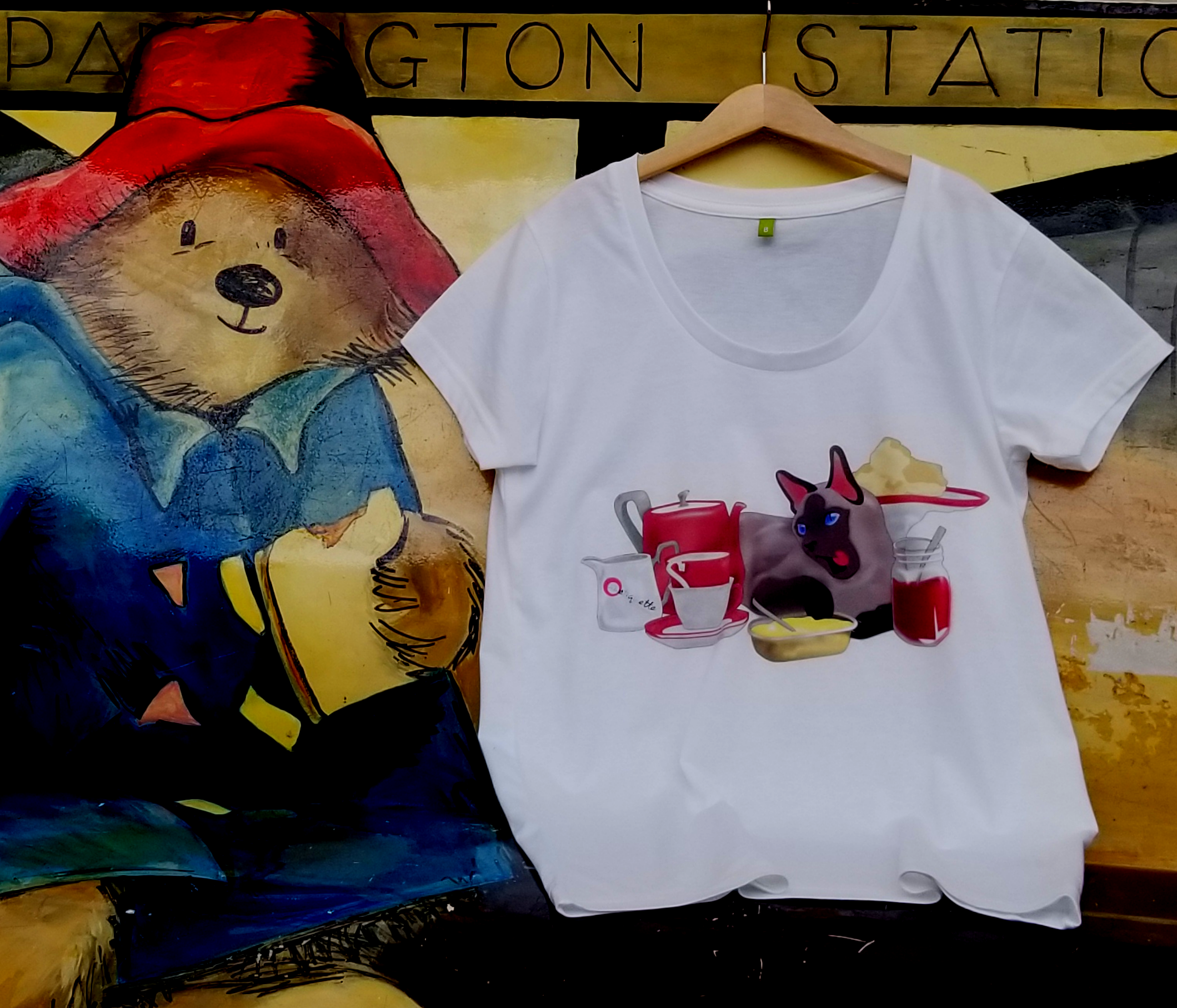 A white t-shirt with Tubetiquette's 'Cream Tea' design next to Paddington Bear with his marmite sandwich.