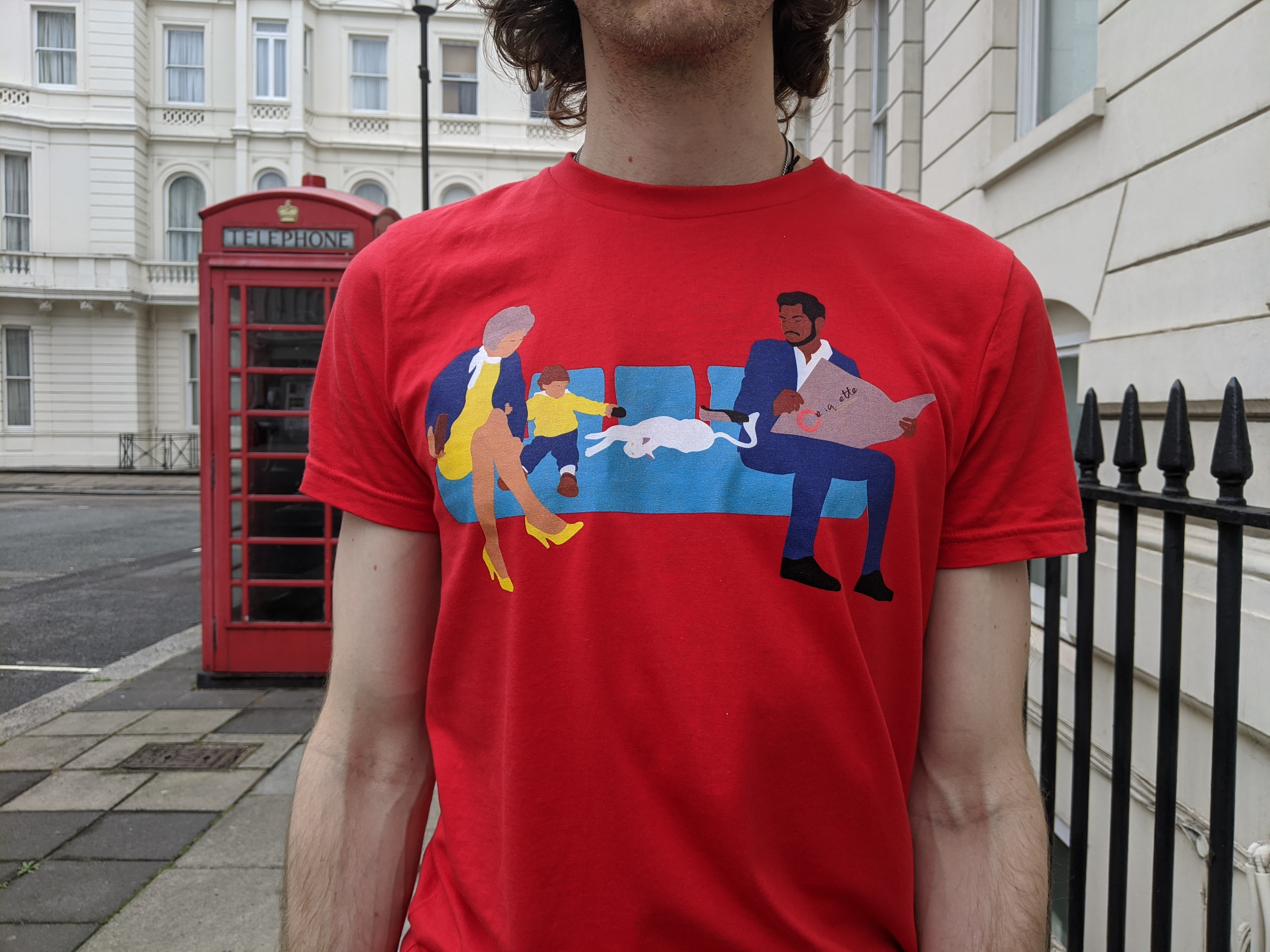 A t-shirt with Tubetiquette's 'Spread' design, in the same red colour as the UK telephone box. The t-shirt features a white cat spreading across a few seats on the London Tube.